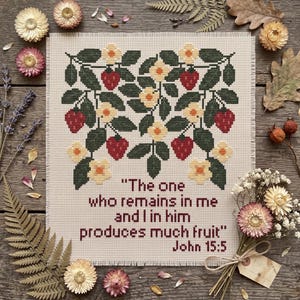 May include: A square piece of beige Aida fabric featuring a cross-stitch pattern of strawberry plants with red berries, dark green leaves, and pale yellow flowers. Below the design, the text reads: "The one who remains in me and I in him produces much fruit" John 15:5.