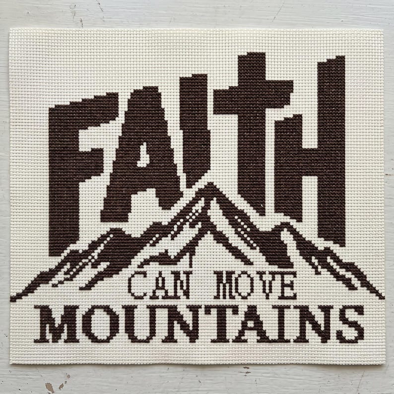 May include: A square cross-stitch embroidery piece on off-white Aida cloth featuring the dark brown text FAITH positioned above a graphic of a mountain range, with the text CAN MOVE MOUNTAINS stitched in dark brown below the mountain design.