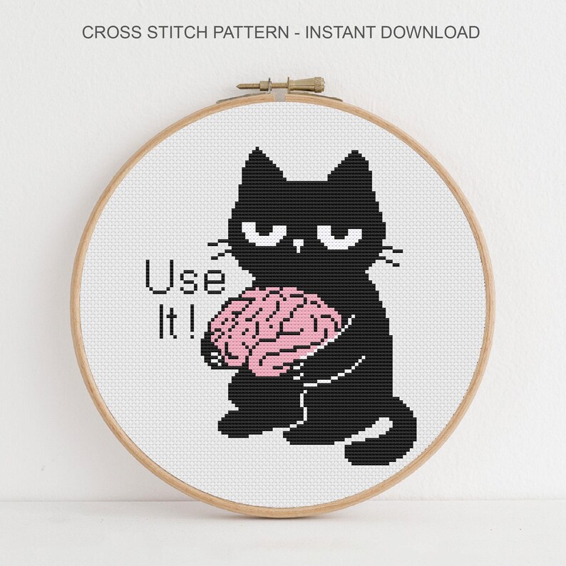 K&ouml;nnte beinhalten: Ein Kreuzstichmuster in einem h&ouml;lzernen Stickrahmen mit einer schwarzen Katze mit m&uuml;rrischem Gesichtsausdruck, die ein rosa Gehirn h&auml;lt. Der Text "Use It!" steht links neben der Katze. Der obere Text lautet "CROSS STITCH PATTERN - INSTANT DOWNLOAD".