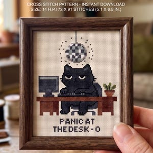 Peut inclure: Un motif de point de croix encadré représentant un chat noir assis à un bureau marron avec un ordinateur et une boule à facettes au-dessus. Le texte indique "PANIC AT THE DESK - O". Le motif mesure 13 x 16,5 cm, 72 x 91 points, 14 H.P.I.