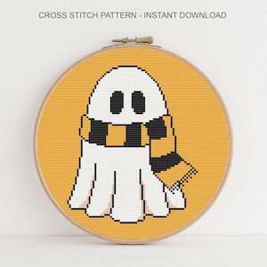Puede incluir: Un patr&oacute;n de punto de cruz con un fantasma blanco con una bufanda negra y dorada, sobre un fondo amarillo. El dise&ntilde;o est&aacute; enmarcado en un bastidor de bordado de madera. El texto en la parte superior dice "CROSS STITCH PATTERN - INSTANT DOWNLOAD."