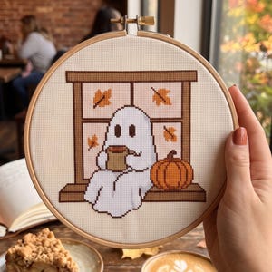 Peut inclure: Un tambour &agrave; broder circulaire en bois contenant un motif au point de croix repr&eacute;sentant un fant&ocirc;me blanc assis sur un rebord de fen&ecirc;tre marron. Le fant&ocirc;me tient une tasse marron, avec une citrouille orange &agrave; c&ocirc;t&eacute;. Des feuilles d'automne pars&egrave;ment.