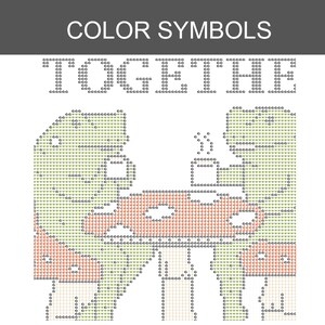Pu&ograve; includere: Uno schema a punto croce intitolato COLOR SYMBOLS con la parola TOGETHER in alto. Il disegno presenta un'illustrazione pixelata di due figure sedute a un tavolo con tazze, resa in tonalit&agrave; di verde, rosso e nero su una griglia bianca.