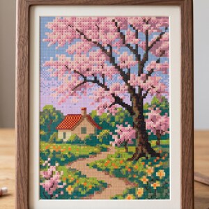 Puede incluir: Obra de arte en punto de cruz enmarcada que representa un paisaje sereno. Un camino conduce a una peque&ntilde;a casa con techo rojo, rodeada de vegetaci&oacute;n y cerezos en flor rosas. El marco es de madera oscura. Aproximadamente 30 cm x 40 cm.