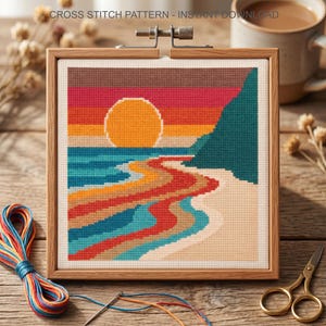 May include: A square cross stitch pattern titled CROSS STITCH PATTERN - INSTANT DOWNLOAD featuring a sunset over a beach with a large orange sun, teal cliffs, and multi-colored waves in shades of red, blue, and yellow, held in a wooden frame.