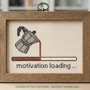 Puede incluir: Arte de punto de cruz en un marco de madera. El diseño presenta una cafetera vertiendo en una barra de progreso marrón con el texto "motivation loading ...". El marco tiene un asa de color latón en la parte superior.