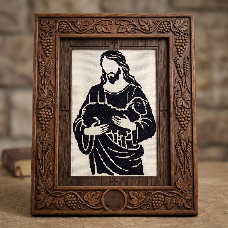 Pode incluir: Uma imagem bordada emoldurada que retrata uma figura religiosa segurando um cordeiro. A obra de arte em preto e branco est&aacute; emoldurada em uma moldura de madeira marrom escura com detalhes esculpidos de uvas e trigo. A moldura tem formato retangular.