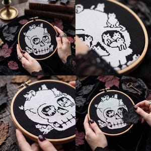 May include: A circular wooden embroidery hoop containing a black fabric piece with a white cross-stitch design of a human skull. The skull is composed of multiple small cat figures, with cats positioned on the cranium, within the eye sockets, and along the jawline.