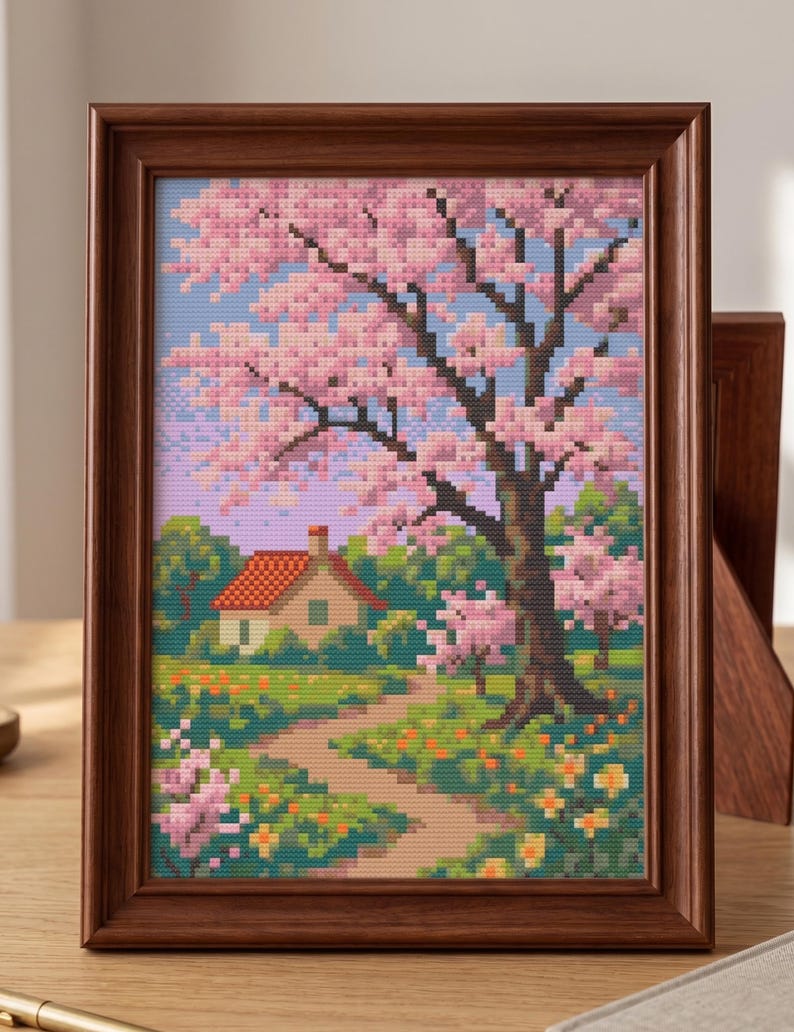Puede incluir: Paisaje en punto de cruz enmarcado que presenta una casa con tejado rojo, un camino y un gran &aacute;rbol con flores rosas. La obra de arte est&aacute; enmarcada en un marco de madera, mostrando una serena escena primaveral con colores vibrantes.