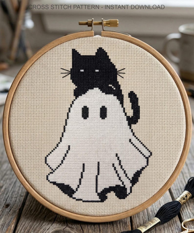 May include: A cross-stitch pattern featuring a black cat perched atop a white ghost. The design is set within a wooden embroidery hoop. The text "CROSS STITCH PATTERN - INSTANT DOWNLOAD" is at the top. Black thread and scissors are visible.