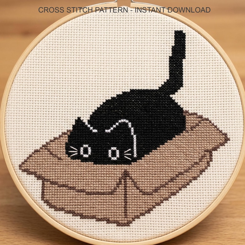 Peut inclure: Un motif de point de croix repr&eacute;sentant un chat noir dans une bo&icirc;te en carton, encadr&eacute; dans un cercle en bois. Le chat a des moustaches et des yeux blancs. Le texte "CROSS STITCH PATTERN - INSTANT DOWNLOAD" est en haut.