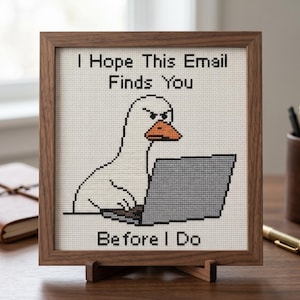 May include: A square cross-stitch embroidery in a brown wooden frame featuring a white goose with an orange beak sitting at a grey laptop. The text reads I Hope This Email Finds You BEFORE I Do in black capital letters against a white fabric background.