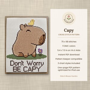 May include: A cross stitch pattern featuring a brown capybara with a yellow bird on its head and a purple flower on green grass. The text reads Don't Worry BE CAPY. The pattern details include 75 x 98 stitches, 11 DMC colours, and 13.7 x 17.8 cm on 14 ct Aida.