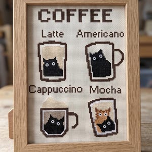 May include: Cross-stitch artwork in a light wood frame. The artwork features the word "COFFEE" above four coffee drink illustrations: Latte, Americano, Cappuccino, and Mocha. Each drink contains a cat.