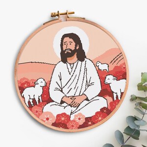 K&ouml;nnte beinhalten: Ein Kreuzstich-Stickrahmen mit einer religi&ouml;sen Szene. Das Design zeigt eine Figur in wei&szlig;en Gew&auml;ndern mit Heiligenschein, umgeben von Schafen und Blumen, vor einer Landschaft in Rot- und Rosat&ouml;nen. Der Holzrahmen ist sichtbar.