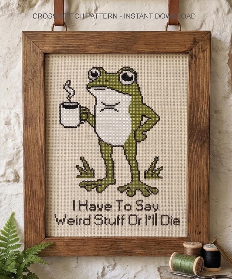 Puede incluir: Un patr&oacute;n de punto de cruz en un marco de madera que muestra una rana verde sosteniendo una taza blanca humeante. El texto debajo de la rana dice, I Have To Say Weird Stuff Or I'll Die. El dise&ntilde;o est&aacute; sobre una tela color crema con cuadr&iacute;cula.