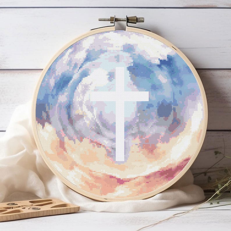 Pode incluir: Bordado em ponto cruz em um bastidor de madeira. O design apresenta uma cruz branca contra um fundo de cores pastel em redemoinho, incluindo azul, roxo e p&ecirc;ssego. A cruz &eacute; o ponto focal da obra.
