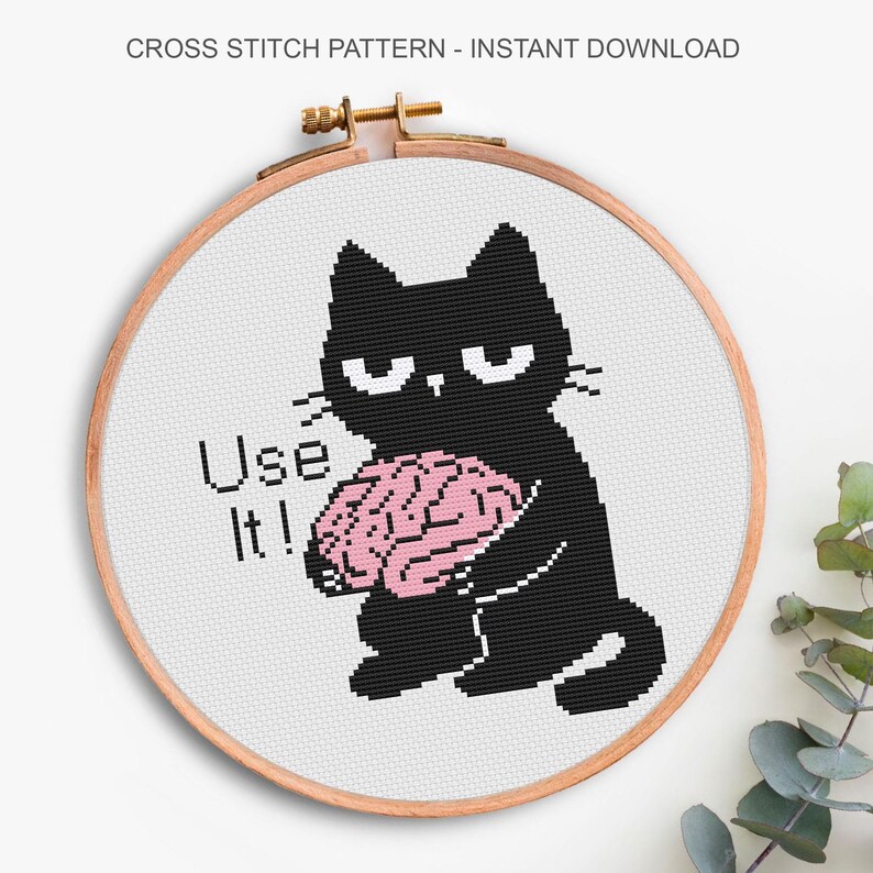 K&ouml;nnte beinhalten: Ein Kreuzstichmuster in einem h&ouml;lzernen Stickrahmen, das eine schwarze Katze mit einem rosa Gehirn zeigt, dazu der in Schwarz gestickte Text Use It!. Das Design befindet sich auf wei&szlig;em Stoff mit dem Text CROSS STITCH PATTERN - INSTANT DOWNLOAD.