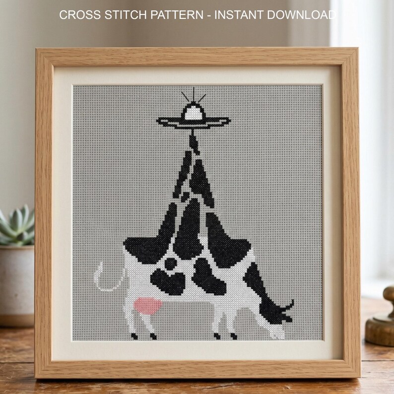 Pode incluir: Padr&atilde;o de ponto cruz emoldurado com uma vaca com manchas pretas e brancas, um &uacute;bere rosa e um OVNI acima. O texto "CROSS STITCH PATTERN - INSTANT DOWNLOAD" est&aacute; no topo. A obra de arte est&aacute; em uma moldura de madeira marrom clara.