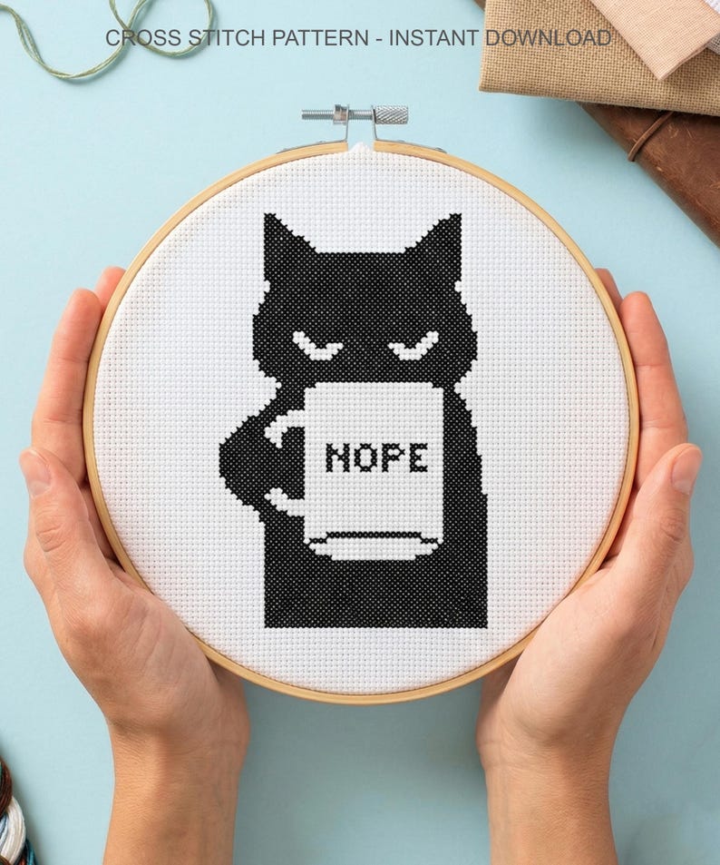 May include: A cross-stitch design in a wooden hoop shows a black cat holding a mug with the word "HOPE". The design is on white fabric. The text "CROSS STITCH PATTERN - INSTANT DOWNLOAD" is at the top. The hoop is held by hands.