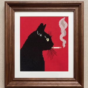 May include: Cross-stitch art of a black cat smoking a cigarette, set against a red background. The cat's silhouette is detailed with yellow eyes and whiskers. The artwork is framed in a dark brown wooden frame.