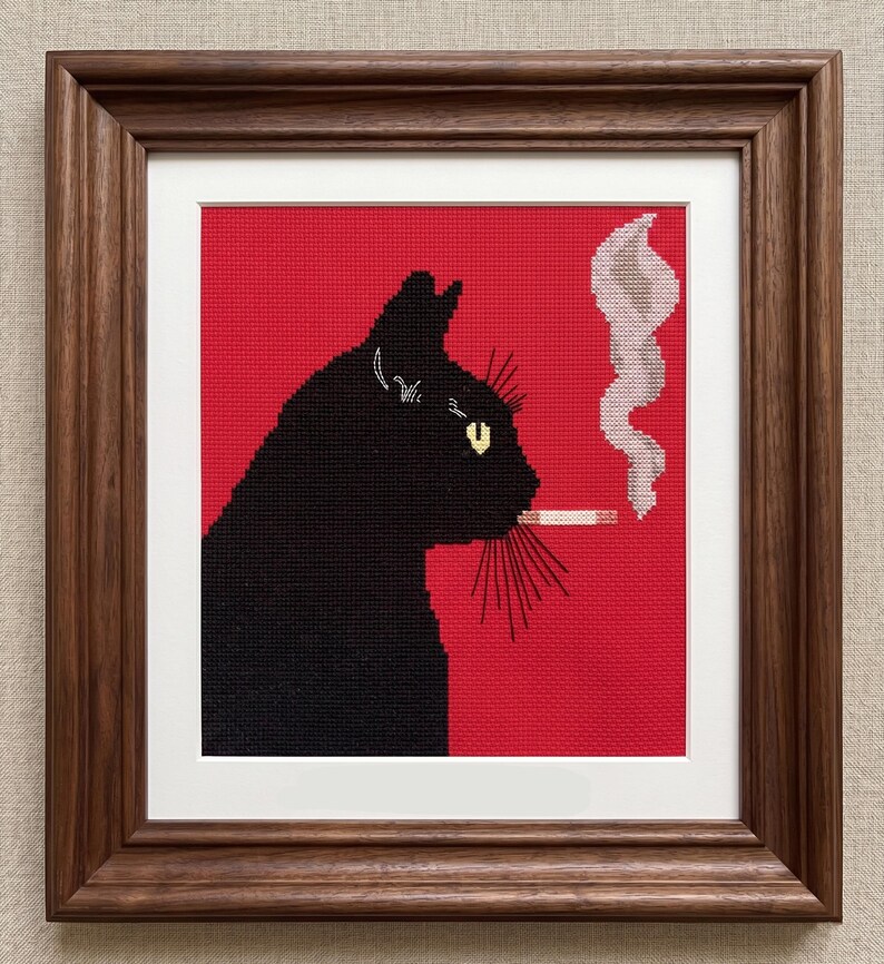 May include: Cross-stitch art of a black cat smoking a cigarette, set against a red background. The cat's silhouette is detailed with yellow eyes and whiskers. The artwork is framed in a dark brown wooden frame.