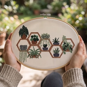 May include: An oval wooden embroidery hoop containing a cross-stitch pattern on white fabric. The design features various green potted plants arranged within interconnected brown hexagonal shelves, showcasing diverse foliage and plant shapes.