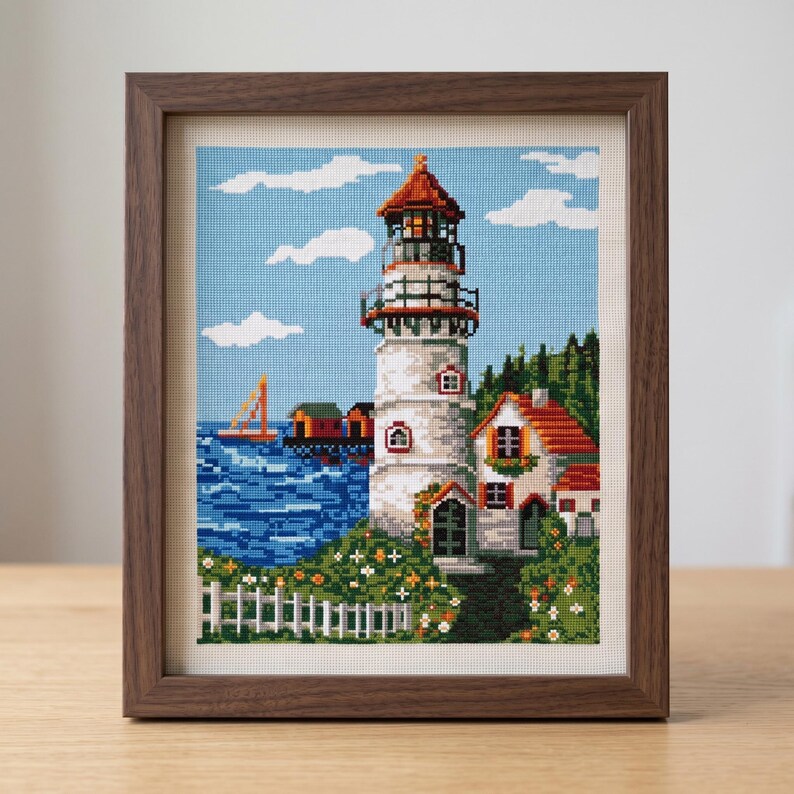 Peut inclure: Une broderie au point de croix encadr&eacute;e repr&eacute;sentant une sc&egrave;ne c&ocirc;ti&egrave;re avec un phare blanc, une maison au toit rouge, une mer bleue avec un voilier et une cl&ocirc;ture blanche. L'&oelig;uvre est ins&eacute;r&eacute;e dans un cadre en bois brun fonc&eacute; textur&eacute;.
