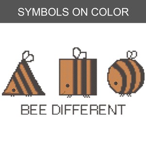 May include: A cross-stitch pattern titled SYMBOLS ON COLOR featuring three geometric bee shapes: a triangle, a square, and a circle, all with orange and black stripes. Below the bees, the text BEE DIFFERENT is displayed in a pixelated font style.