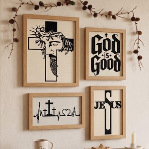 Puede incluir: Cuatro obras de punto de cruz en marcos de madera clara. Una muestra un rostro con corona de espinas sobre una cruz, otra dice God is Good, otra muestra una l&iacute;nea de latido con cruces y un coraz&oacute;n, y otra presenta la palabra JESUS en una cruz.
