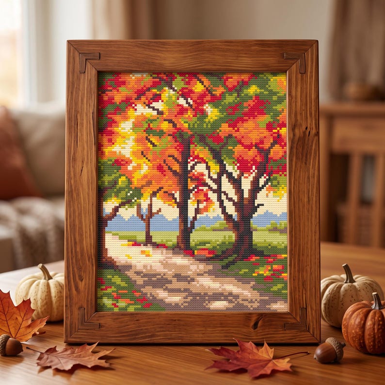 Puede incluir: Un bordado de punto de cruz que representa un paisaje oto&ntilde;al con &aacute;rboles de colores rojo, naranja y amarillo vibrantes a lo largo de un camino, enmarcado en un marco de madera rectangular. La escena muestra un cielo azul claro y hierba verde.