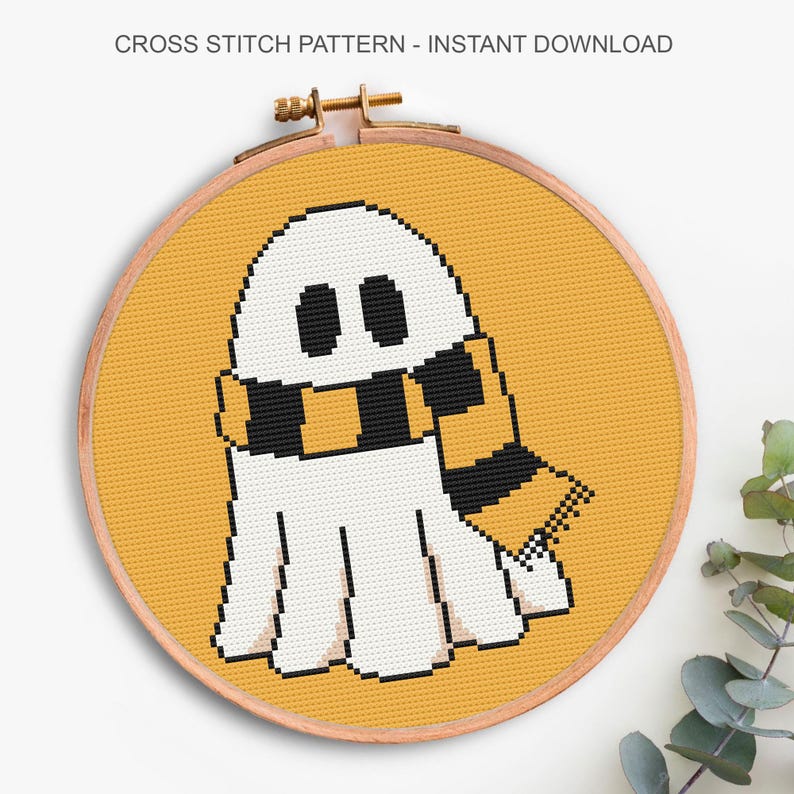 Puede incluir: Patr&oacute;n de punto de cruz de un fantasma blanco con una bufanda negra y dorada, sobre un fondo amarillo, en un c&iacute;rculo y un aro de madera. El texto en la parte superior dice "CROSS STITCH PATTERN - INSTANT DOWNLOAD". Ideal para manualidades.