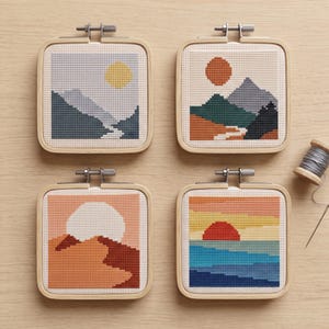 Peut inclure: Quatre tambours &agrave; broder carr&eacute;s pr&eacute;sentant des paysages au point de croix. En haut &agrave; gauche, un soleil jaune sur des montagnes bleues. En haut &agrave; droite, un soleil orange sur des sommets multicolores. En bas &agrave; gauche, un soleil blanc sur des dunes orange. En bas &agrave; droite, un soleil rouge sur une mer bleue.