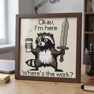 Puede incluir: Imagen de punto de cruz enmarcada en madera oscura. Muestra un mapache sosteniendo una taza de caf&eacute; y una espada. El texto dice: "Okay, I'm here" y "Where's the work?" El mapache es marr&oacute;n, negro y blanco.