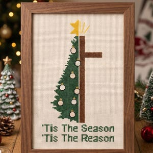 K&ouml;nnte beinhalten: Ein gerahmtes Kreuzstichmuster mit einem Weihnachtsbaum-Design, kombiniert mit einem Kreuz. Der Baum ist gr&uuml;n mit wei&szlig;en Kugeln, und das Kreuz ist braun. Der Text "'Tis The Season, 'Tis The Reason" steht unten. Der Rahmen ist aus Holz.