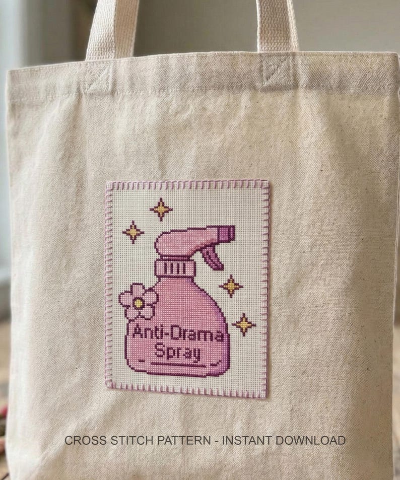 Peut inclure: Sac fourre-tout beige avec un patch en point de croix repr&eacute;sentant un vaporisateur rose. Le patch indique "Anti-Drama Spray" avec des fleurs et des &eacute;toiles. Les mots "CROSS STITCH PATTERN - INSTANT DOWNLOAD" sont en bas.