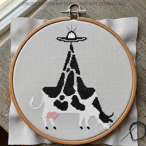 Pode incluir: Um padr&atilde;o de ponto cruz de uma vaca com manchas pretas e brancas e um OVNI acima. O design est&aacute; num bastidor de bordado de madeira, com o texto "CROSS STITCH PATTERN - INSTANT DOWNLOAD" no topo. Uma agulha e linha s&atilde;o vis&iacute;veis.