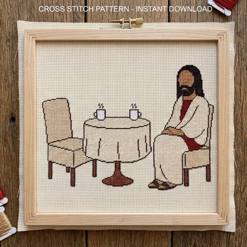 May include: Cross-stitch pattern featuring a religious figure seated at a table with two cups of coffee. The design includes a table, two chairs, and the text "CROSS STITCH PATTERN - INSTANT DOWNLOAD" at the top. The artwork is framed in a wooden hoop.