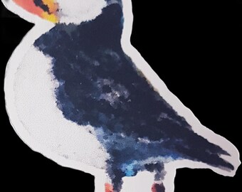 May include: A watercolor-style illustration of a puffin bird. The bird has a white belly, a dark blue back, and a large, colorful beak with red, yellow, and orange hues. The background is solid black.