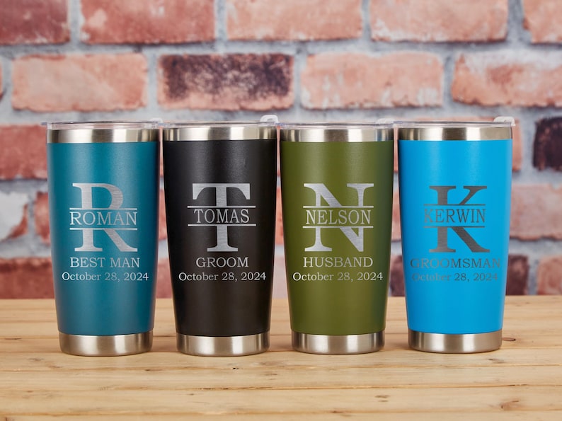 May include: Four personalized stainless steel tumblers in teal, black, olive green, and blue. Each tumbler features a name and title, with the date "October 28, 2024" engraved below. The tumblers are on a wooden surface.