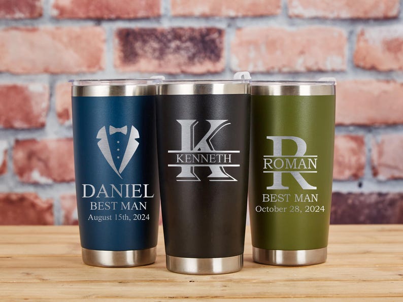 May include: Three personalized stainless steel tumblers in navy blue, black, and olive green. Each tumbler features custom text and a design, including a tuxedo graphic and initials. The tumblers are designed for a wedding party.