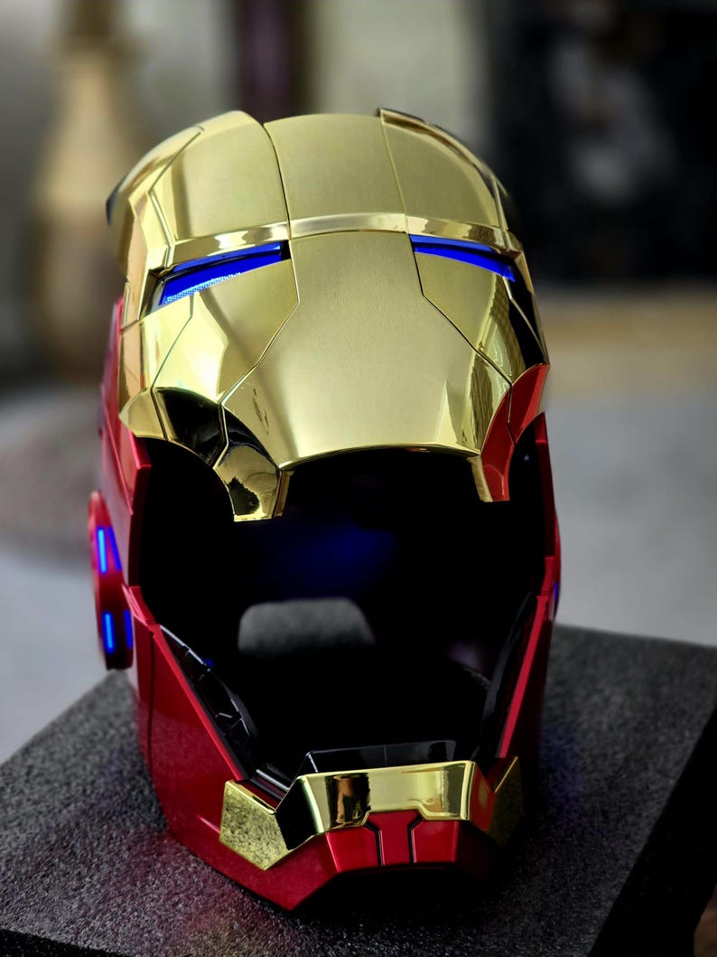 May include: A gold and red Iron Man helmet with a black visor and blue lights. The helmet is made of plastic and has a detailed design.