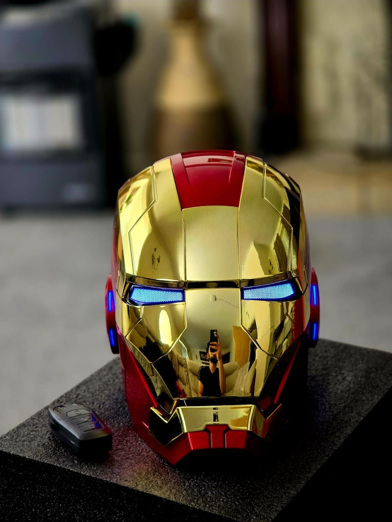 May include: A gold and red Iron Man helmet with blue LED lights. The helmet is made of plastic and has a glossy finish.