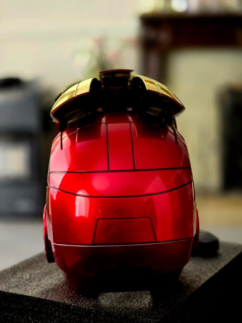 May include: A red and gold Iron Man helmet replica. The helmet is made of plastic and has a shiny finish. The helmet is closed and the faceplate is down.