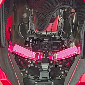 May include: An internal view of a red helmet with a black mesh lining. The helmet features a black and silver mechanism with two pink lights on either side.