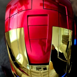 May include: A red and gold helmet with a shiny finish. The helmet has a raised design on the top and a blue trim around the bottom.