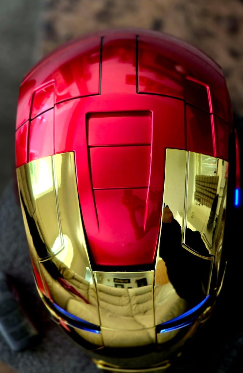 May include: A red and gold helmet with a shiny finish. The helmet has a raised design on the top and a blue trim around the bottom.