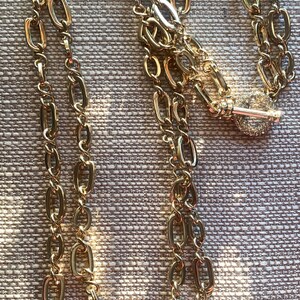 May include: A gold chain necklace with a key pendant. The chain is made of two different sizes of oval links.