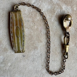 May include: Antique gold-toned watch chain with a rectangular fob and a decorative hand-shaped clasp. The fob features vertical lines and an oval center. The chain is made of small, linked metal pieces.