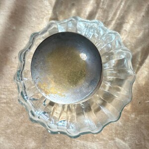Puede incluir: Un tap&oacute;n de botella de vidrio transparente con una parte superior plateada ligeramente deslustrada. La base de vidrio tiene un dise&ntilde;o acanalado y festoneado. El tap&oacute;n es probablemente para una botella de vino o licor.